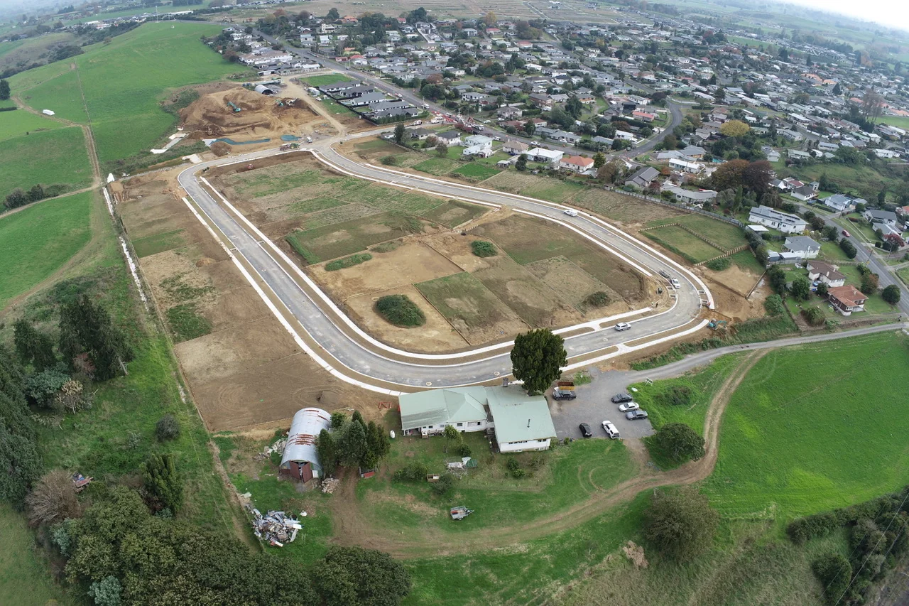 Aerial view of a new R2 Developments subdivision under construction, roads and lots laid out beside existing homes